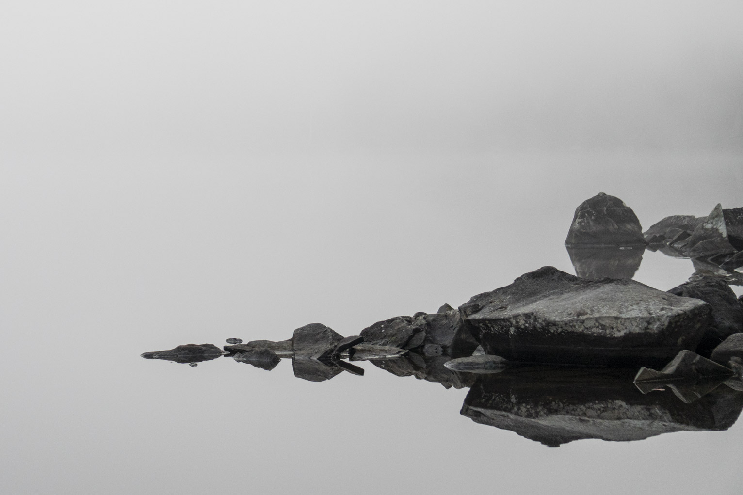 Grey slate reflected in white water, behind all white because of the fog